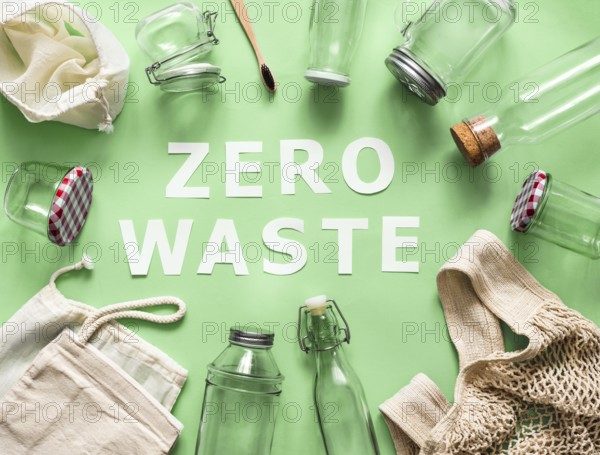 Zero waste concept. Textile eco bags, glass jars and bamboo toothbrush on green background with Zero Waste white paper text in center. Eco friendly and reuse concept. Top view or flat lay