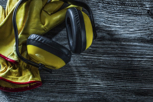 Protective earmuffs leather gloves on wooden board