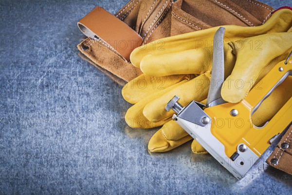 Composition of leather tool belt safety gloves stapler gun on metallic background construction concept