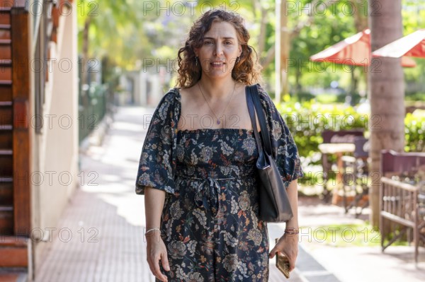 Portrait of a mid-adult woman holding a smartphonewhile looking at the camera on a sunny day