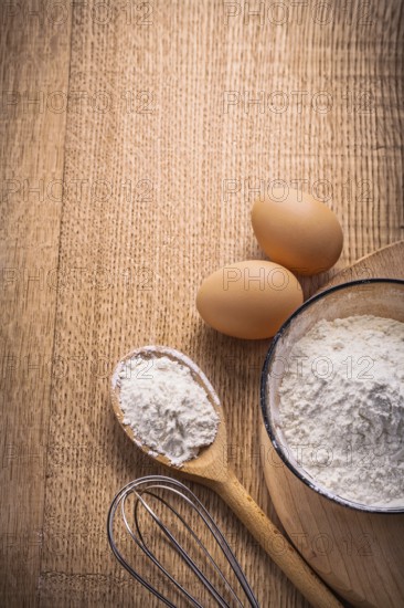 Vertical aerial view organized copyspace eggs flour in bowl spoon corolla on wooden board food and drink concept