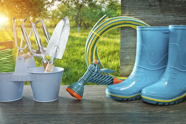 Gardening tools blue rubber rain boots hose sprayer gun spade and fork on vintage table in spring sunny garden at sunrise