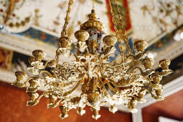 Close-up of an antique gold Italian chandelier. A chandelier-chandelier on gilded chains hangs against the background of the painted ceiling.