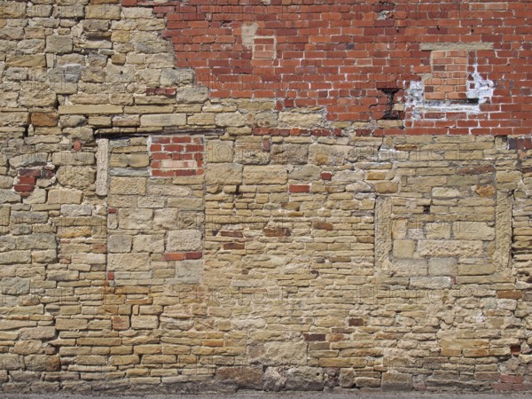 An old exterior wall with an irregular patched and repaired brick and stone surface