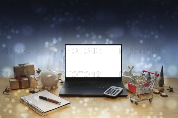 Laptop mockup, online sale offers like Black Friday, table with Christmas decoration, gifts, calculator, shopping cart, piggy bank and notepad, dark blue bokeh background, copy space