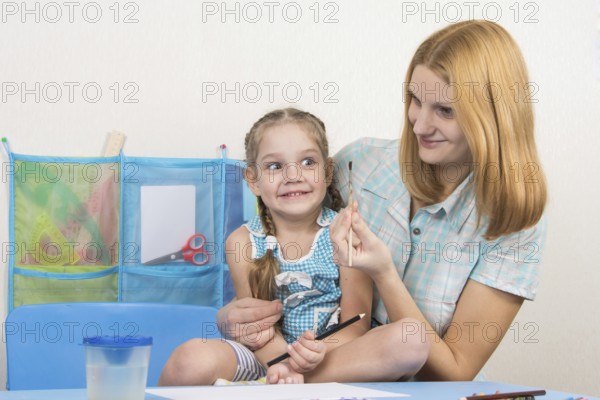 A five-year girl is engaged in drawing with adult young beautiful girl sitting at the children table at home