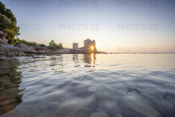 Castle ruins at dawn. Bay on the Mediterranean Sea with calm water at sunrise. Reflection of the sky and the Mediterranean landscape of Kastelina Castle, Vir Island, Zadar, Dalmatia, Croatia, Adriatic Sea, Europe