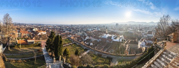 Wide panorama of Graz City, City rooftops, Mur river and city center, Schlossberg hill and clock tower Sun in winter, blue sky. Travel destination