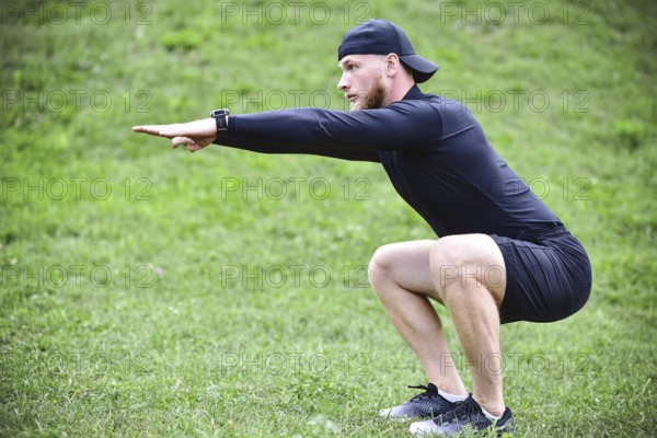 Full length of young concentrated sportsman doing squats outdoors