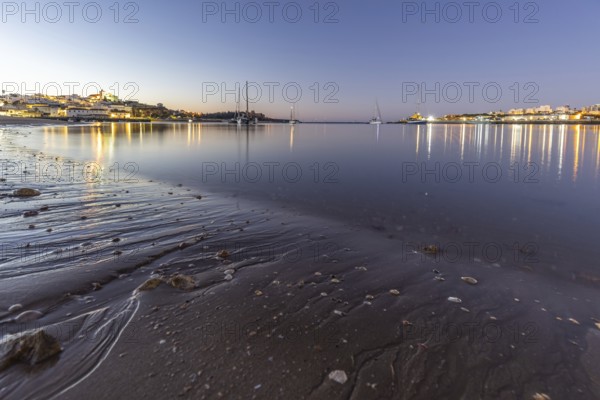 Night shot of a sandy beach and harbour at low tide. Panoramic image of an illuminated historic city centre at dawn in Ferragudo, Portimão, Algarve, Portugal, Europe