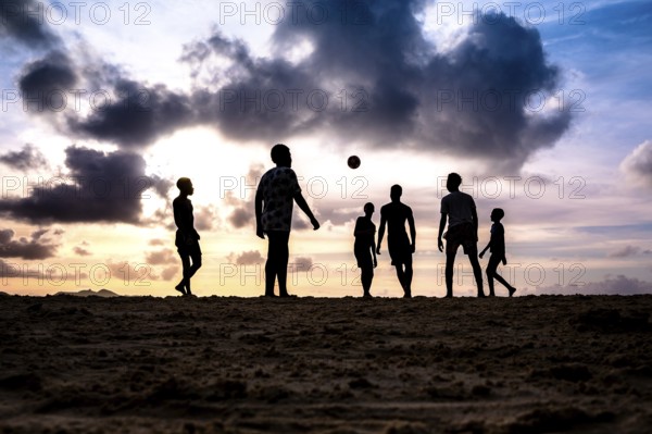 Group of people enjoying a football match on the beach at sunset, silhouettes against a backdrop of clouds, La Digue, Seychelles, Africa