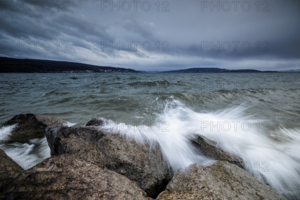 Sprayed waves crash against stones in front of a cloudy sky, harbour, Mittelzell, Reichenau, Lake Constance, Baden-Württemberg, Germany, Europe