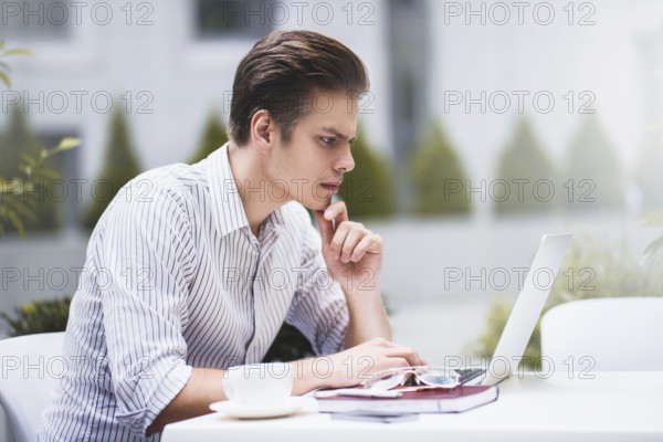 Smart attitude. Positive handsome man using a laptop and sitting in the cafe while surfing the internet