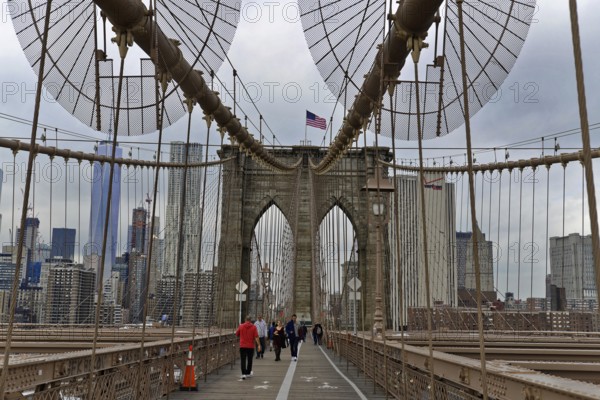 Brooklyn Bridge in Brooklyn, Manhattan, New York, USA United States of America, Brooklyn Bridge with passers-by and the American flag in an urban environment, New York City, USA, North America