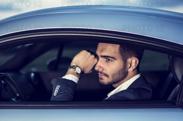 Portrait of young attractiave man in business suit sitting in his new stylish car outdoor in countryside