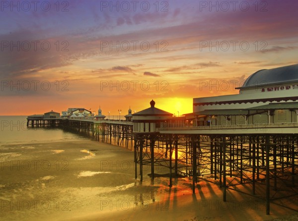 The sun setting over the historic north pier in blackpool with glowing golden light reflected on the beach and colourful twilight sky