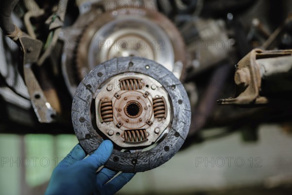 Clutch plate shown by a hand in blue glove in an automotive repair setting