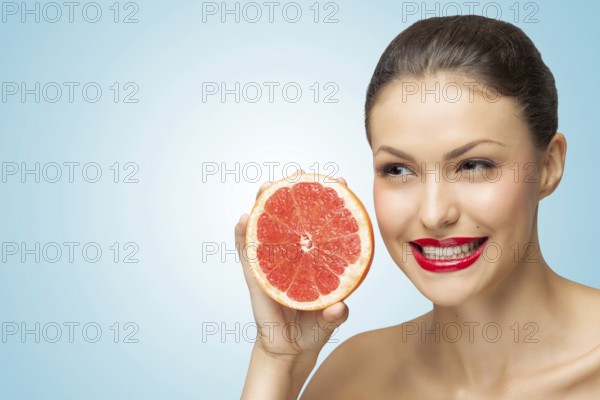 A creative portrait of a beautiful girl holding a red grapefruit sexually under her chin