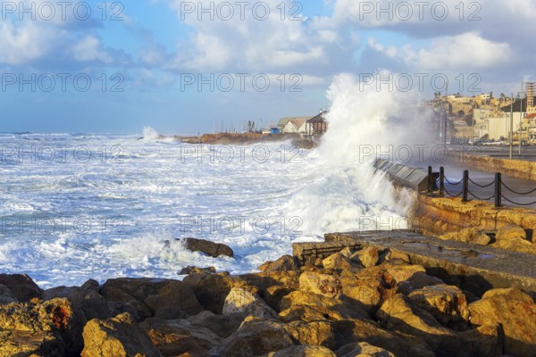 Huge stones protect the coast from huge storm waves. Powerful winter surf takes off with snow-white foam. Embankment in Tel Aviv. Sunset. Windy sunny day on the Mediterranean. Israel