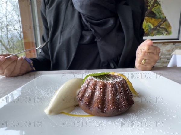 Woman Eating on a White Plate With an Elegant Warm Dark Chocolate Cake Dessert With Vanilla Ice Cream and one Mint Leaf in Switzerland.