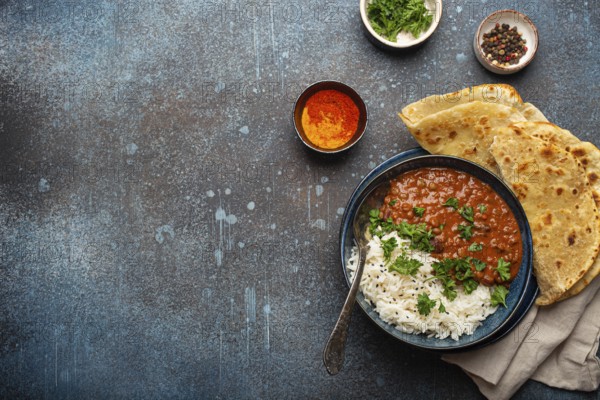 Traditional Indian Punjabi dish Dal makhani with lentils and beans in black bowl served with basmati rice, naan flat bread, fresh cilantro and spoon on blue concrete rustic table top view. Copy space, food photography, food photography