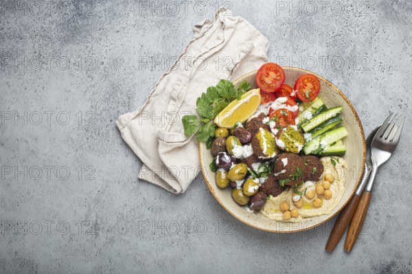 Falafel salad bowl with hummus, vegetables, olives, herbs and yogurt sauce. Vegan lunch plate top view on rustic stone background, healthy meal with falafel and veggies, space for text, food photography, food photography
