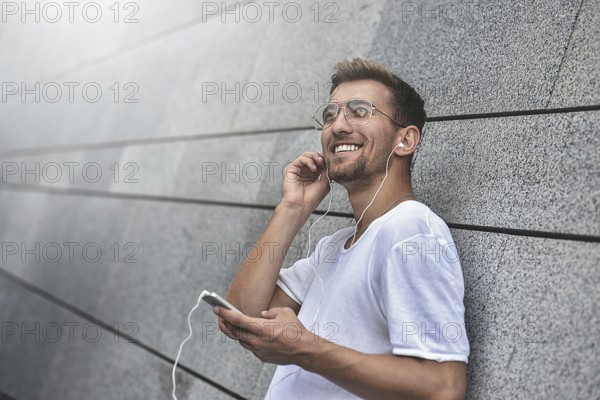 Earphones concept. People, technology, travel and tourism, man with earphones, smartphone on city street and listening to music over gray wall background