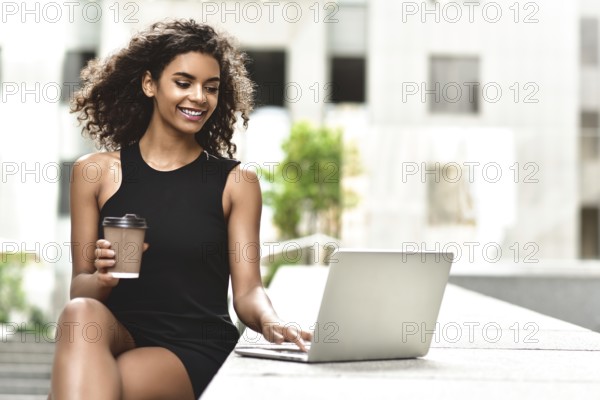 Young attractive Mixed-race girl with beautiful afro hair who is smiling looking at her laptop screen during video call. Young woman using laptop