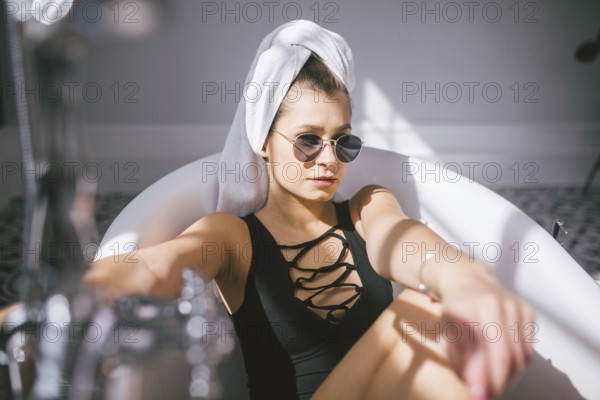 Young caucasian woman with towel on head and sunglasses getting spa treatment in a beauty salon, inside an interior room. Relaxing in the bathroom in linen. The concept of body care and relaxation