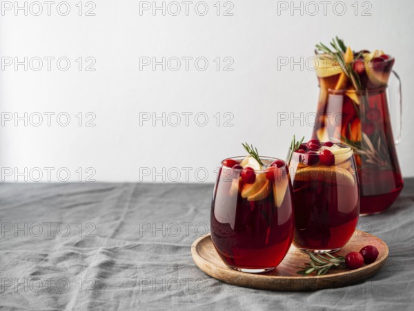 Winter sangria on tabletop with gray linen tablecloth. Jugful of sangria and glasses with with fruit slice, cranberry and rosemary. Copy space for text or design. Horizontal. Top view or flat lay