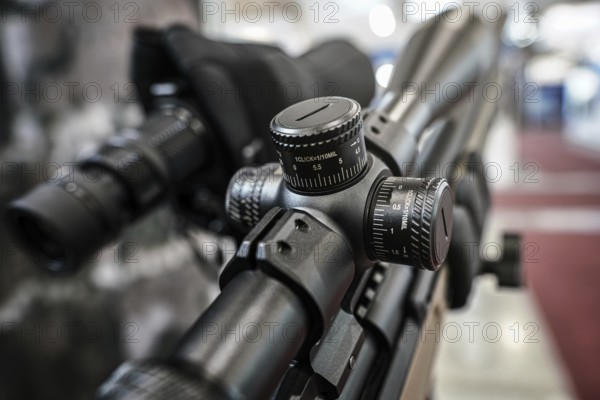 Black shooting scope optics mounted on rifle displayed at weapons exhibition fair, closeup detail to adjustment knobs