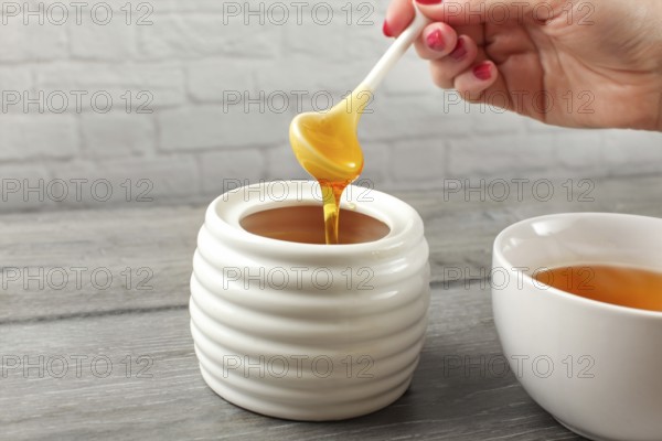 Detail on woman holding small ceramic spoon, filled with honey, about to put it in white tea cup full of hot tea