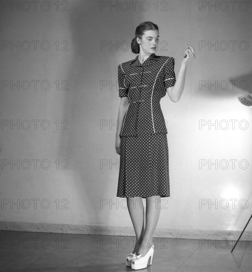 Fashion 1946, a young female model dressed in the fashion of the post war era. The dress with short sleeves reaching below the knees is in dark fabric with a pattern of white dots. Kristoffersson ref Y86-6