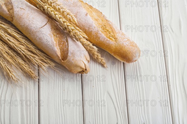 Two baguettes and ears of wheat on old white wooden boards with copyspace