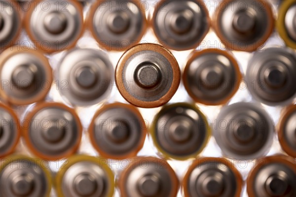Multiple used AA alkaline batteries are seen arranged in a pile. Closeup front view from the plus side of the battery