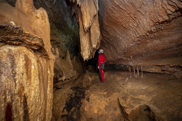 A speleologist with helmet and headlamp exploring a cave with rich stalactite and stalagmite formations. graphy