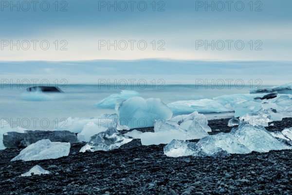 Ice formations along the ocean shoreline under a serene blue sky, creating a cold feeling, Expansive icy scene with glaciers and rugged mountains, capturing a serene, cold atmosphere, iceberg, glacier, snow, ice rock, ice diamont, glacier lagoon, nature, snow, diamont beach, Iceland, Europe