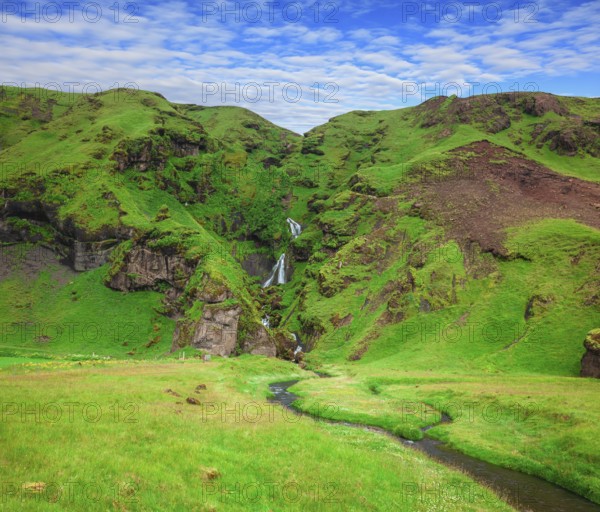 Basalt mountains covered in green moss and grass . Gorgeous cascading waterfall from melting glacier. Iceland
