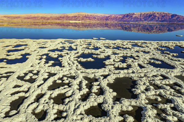 Dead Sea. The blue water is surrounded by pink mountains. Sunny winter day. The picture was taken by a drone from a aerial view. Evaporated salt forms bizarre patterns on the water. Israel
