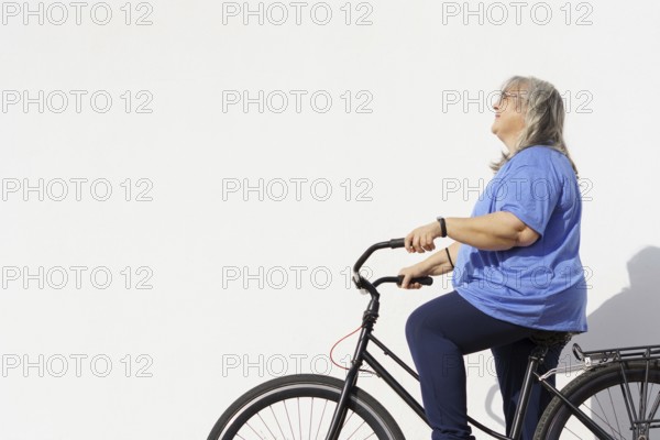 Smiling overweight mature woman riding a retro style bicycle isolated on white background and copy space, exercise concept in the elderly