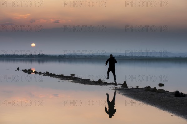 Unrecognised person running to reach the sun. Idyllic winter sunset at a lake. Silhouette reflection on water, Larnaca Cyprus