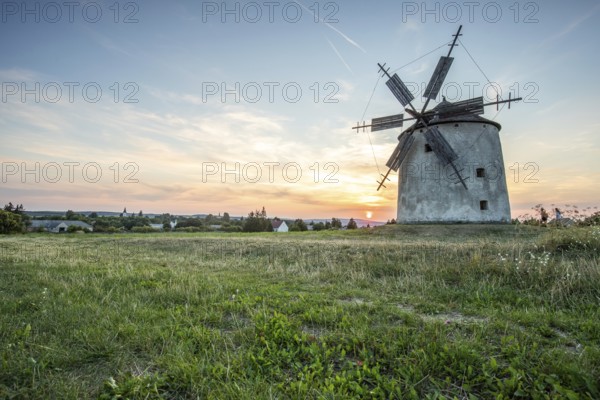 Windmill with wooden sails in a landscape with fields. Meadows and flowers appear in the sunset. Landscape shot in nature with a windmill. Historically atypical for the Balaton region in Hungary
