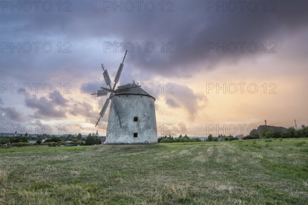 Windmill with wooden sails in a landscape with fields. Meadows and flowers appear in the sunset. Landscape shot in nature with a windmill. Historically atypical for the Balaton region in Hungary