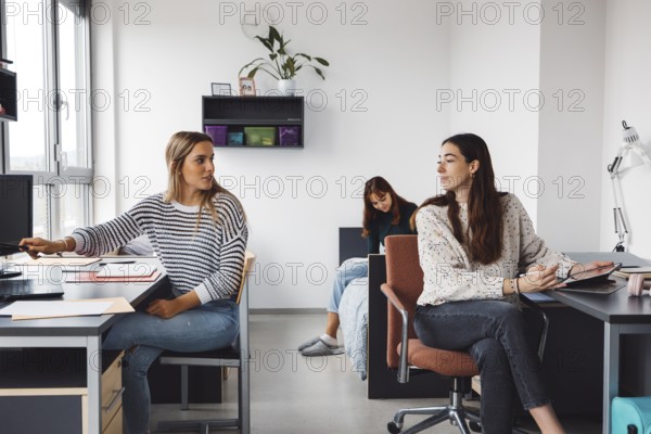 Group of three roommates, college student, young caucasian women, spending time together in their room, studying, talking, having fun, laughing