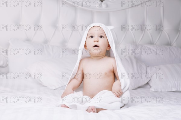 Adorable newborn baby boy with brown eyes sitting wrapped in a white towel with ears in light bed. A happy childhood and the concept of health. Joyful, happy, emotional. beautiful baby