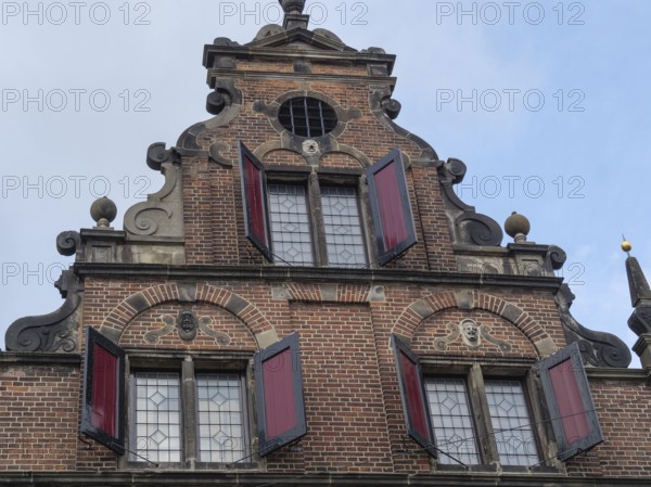 Historic brick façade with decorative elements and red shutters against a cloudy sky, nijmegen, the netherlands