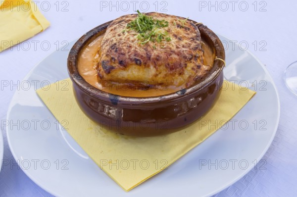 Portion of lasagna bolognese in a terracotta ramekin lay on a white plate