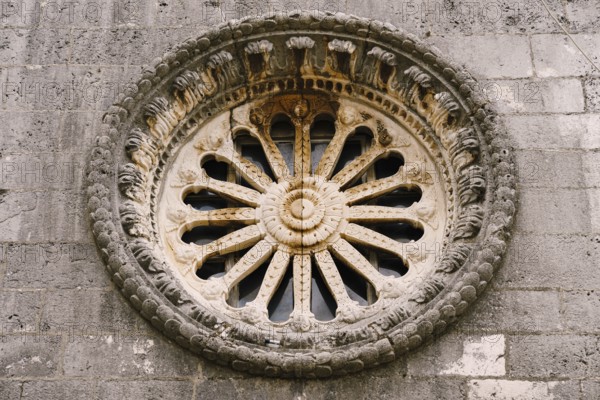 Rose window with ornaments and patterns on the dark stone wall of the church.