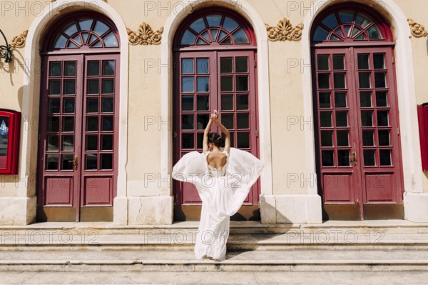 Sibenik, Croatia - 05.06.17: Bride in a white dress fluttering in the wind stands in front of high glass doors to an ancient building