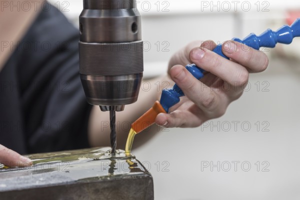 Skilled worker drills hole in steel with metal drill using cooling lubricant